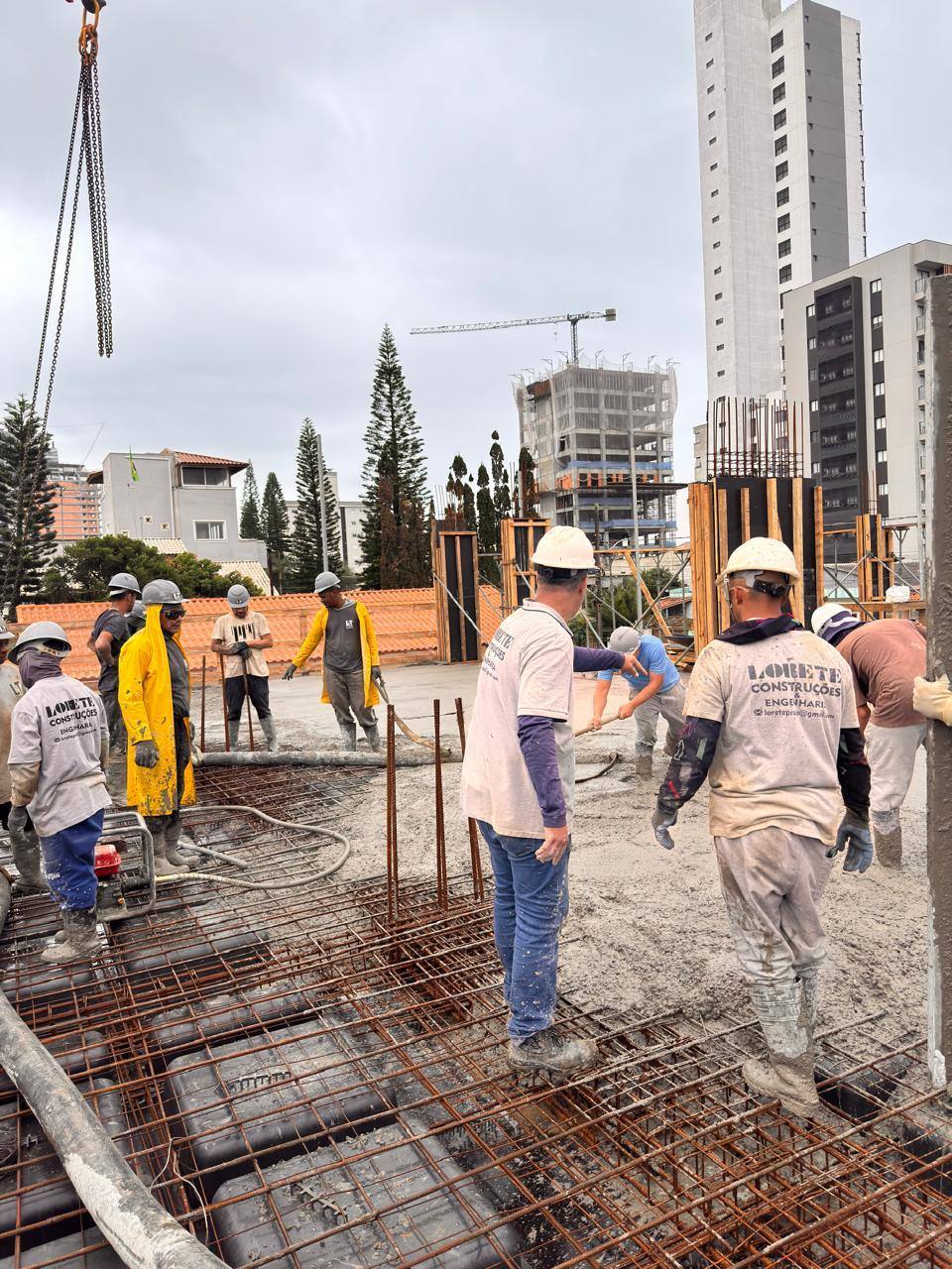 Equipe da Lorete Construções trabalhando sobre a laje, com a grua e torres ao fundo